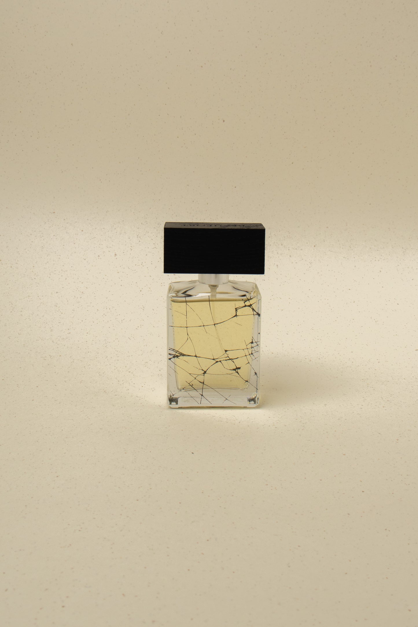 Minimalist perfume bottle with light amber liquid and black stopper on beige speckled background
