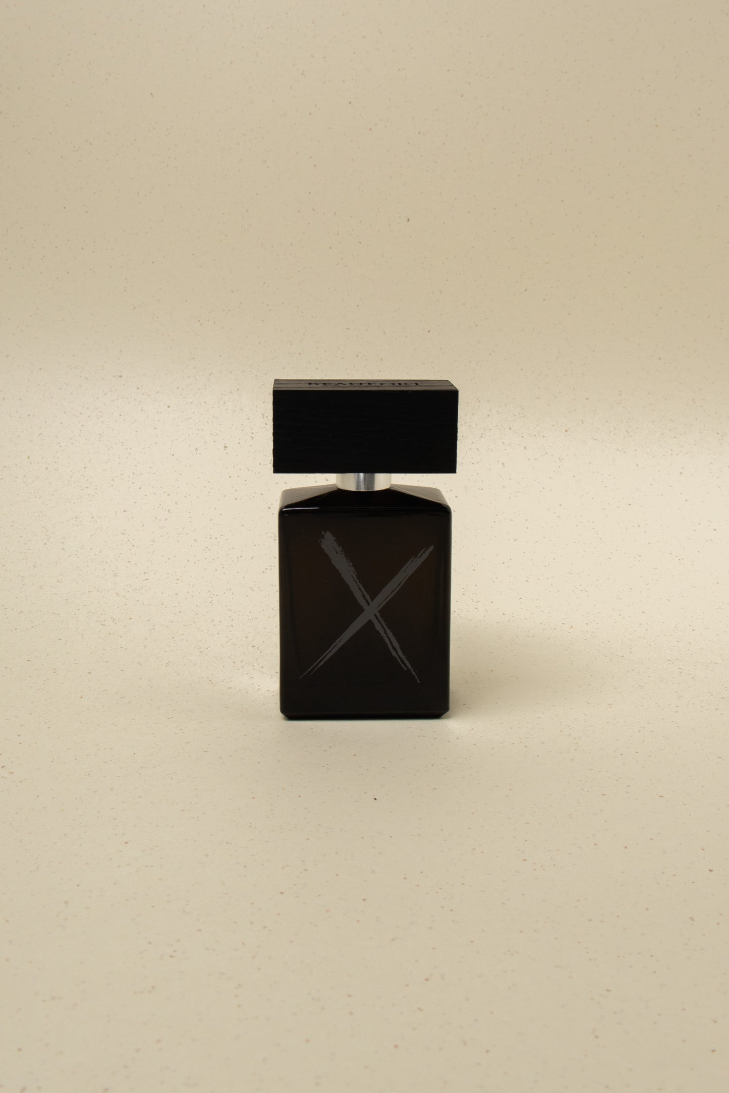 Dark glass perfume bottle with black wooden cap and gray X design on beige background