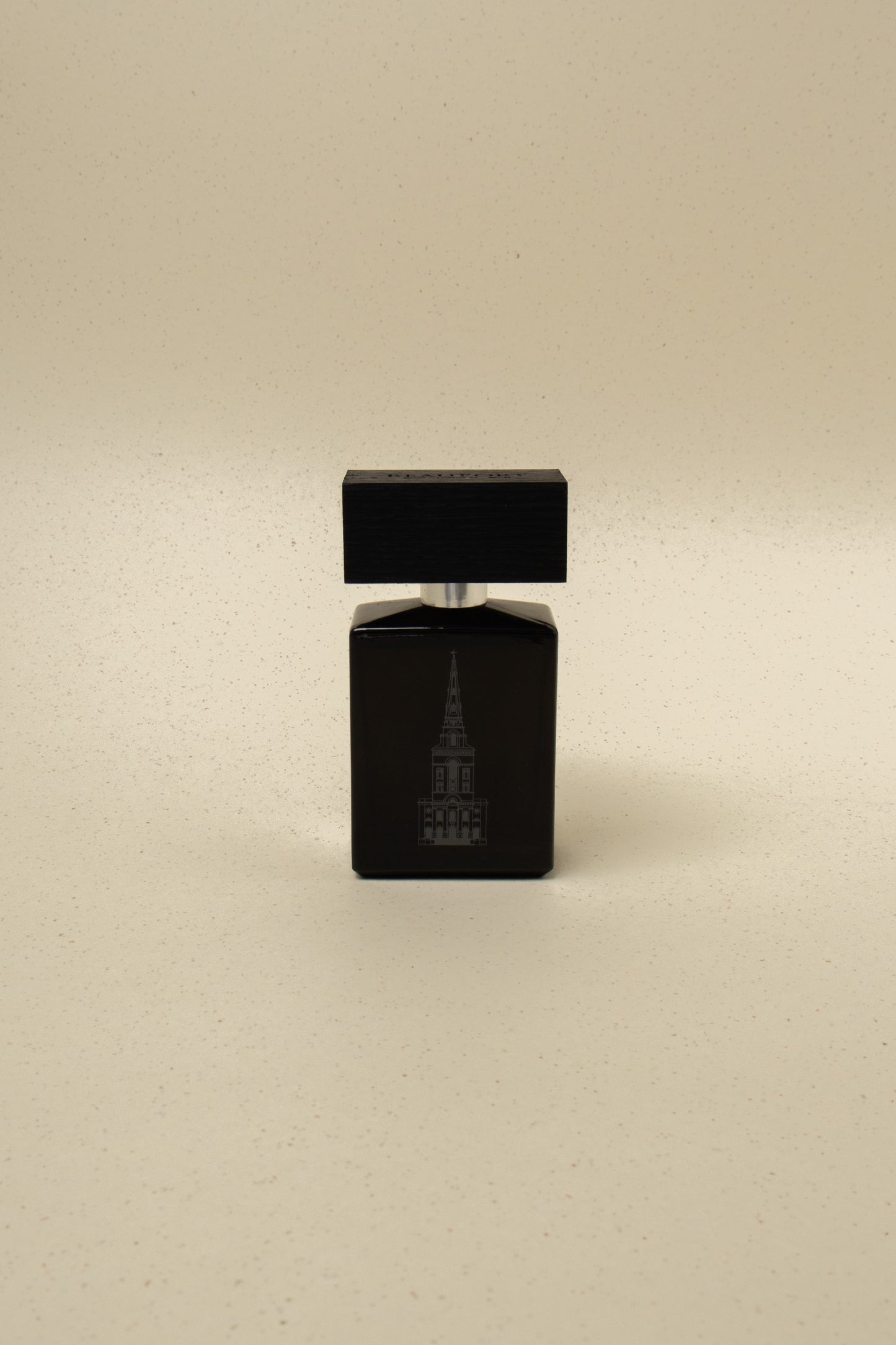 Black perfume bottle with wooden cap featuring a building illustration, on beige speckled background