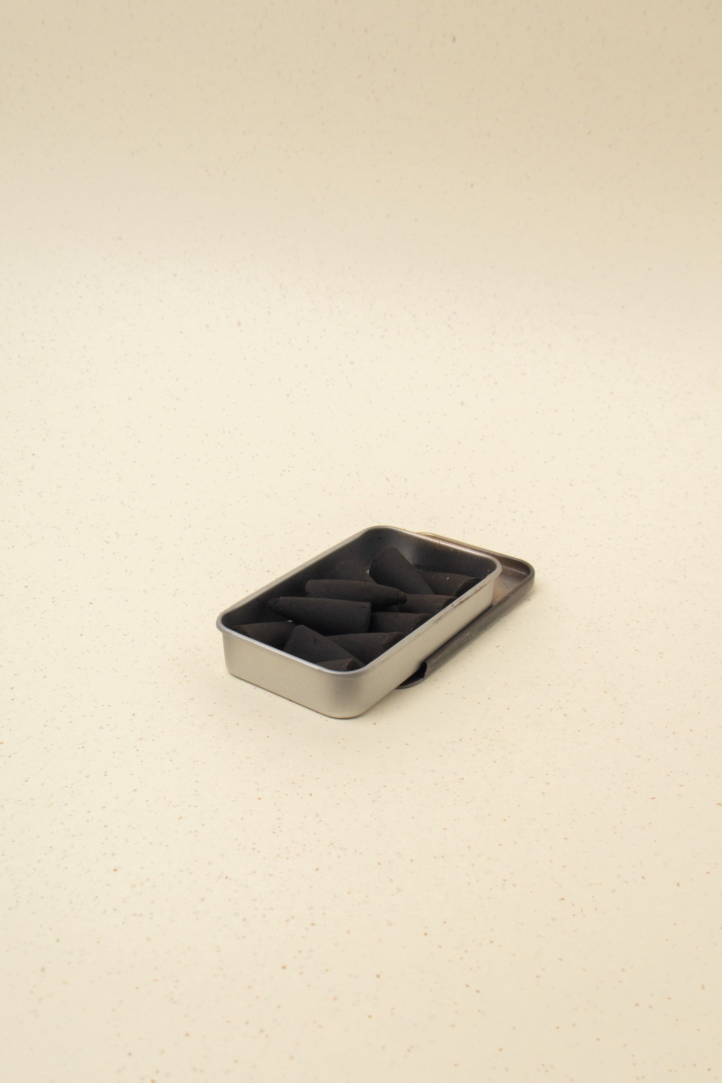 Silver tin container filled with black incense cones on beige speckled surface
