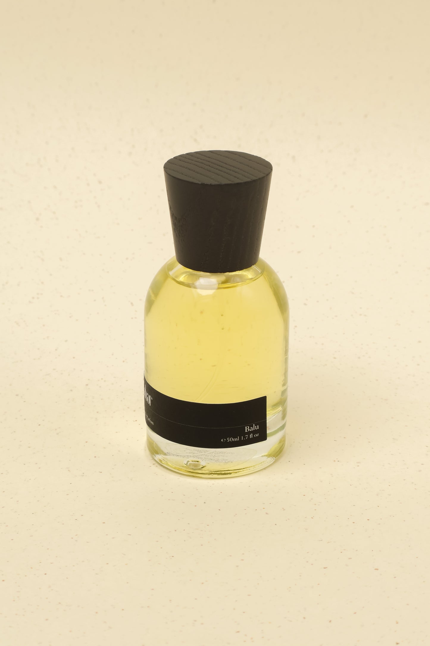 Scented Balu niche perfume bottle with yellow liquid and black cap on beige background