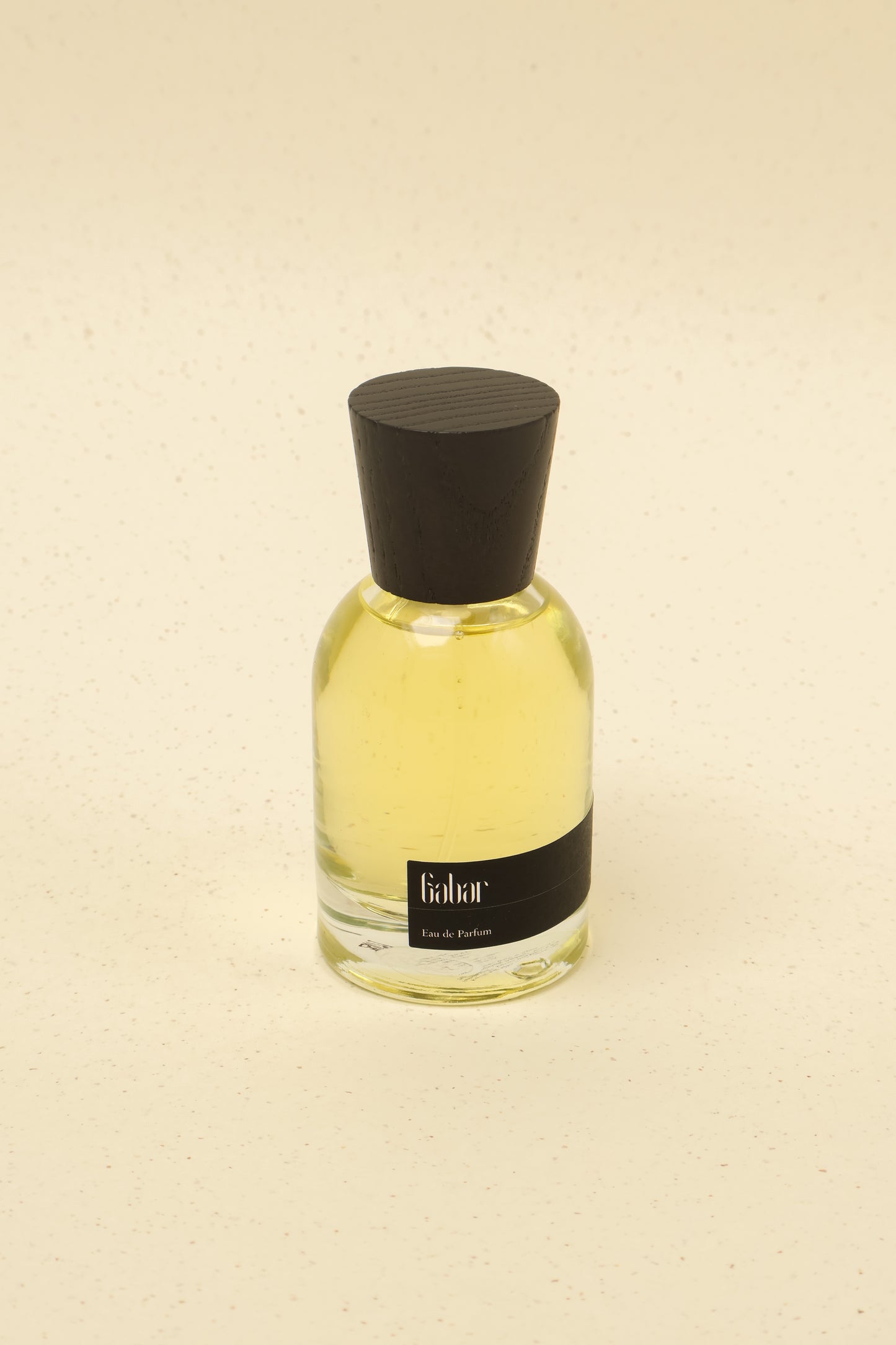 Gabar Eau de Parfum glass bottle with yellow fragrance and dark wooden cap on beige speckled background