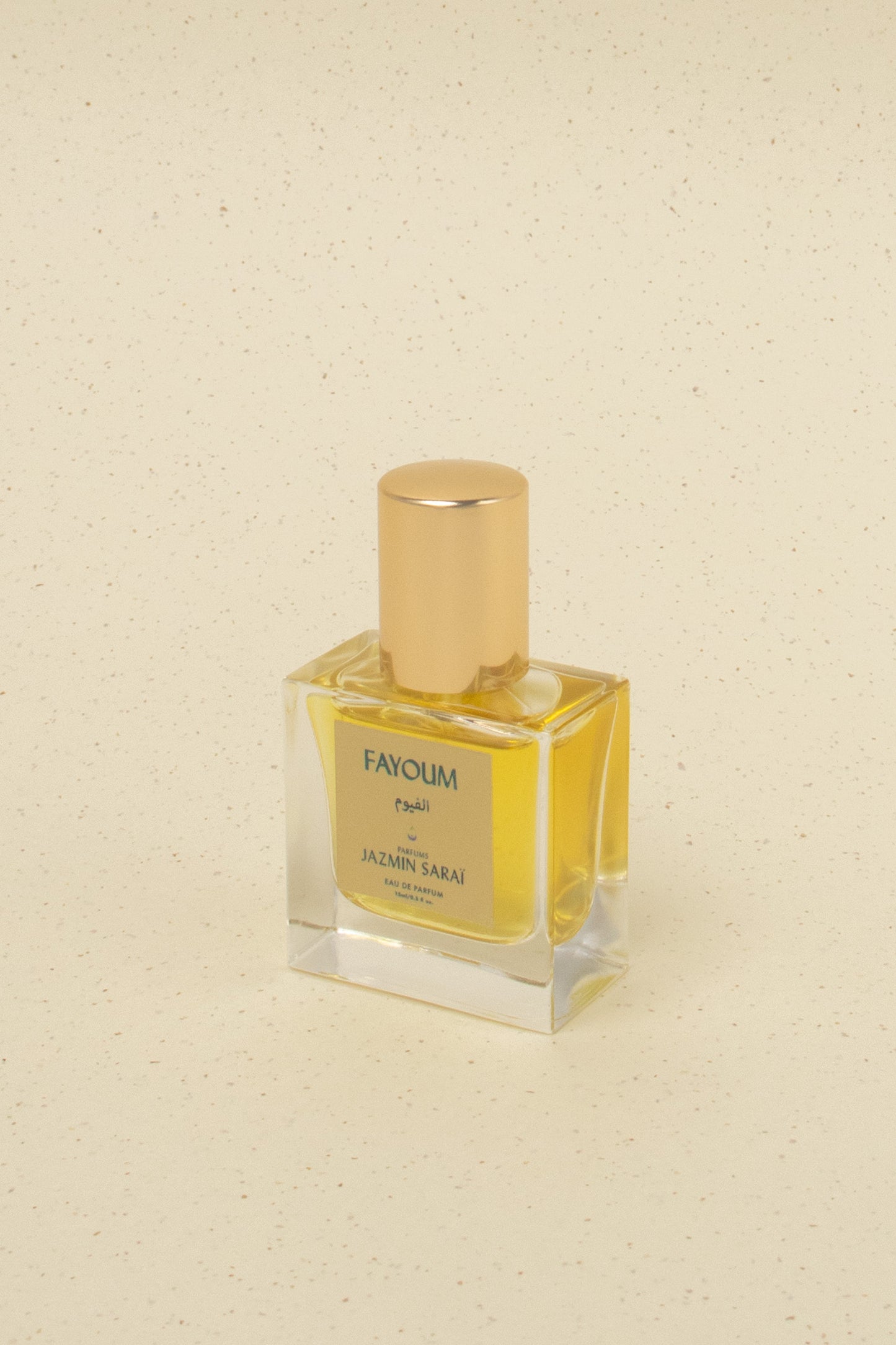 Jazmin Sarai Fayoum eau de parfum in clear square bottle with gold cap on beige speckled background