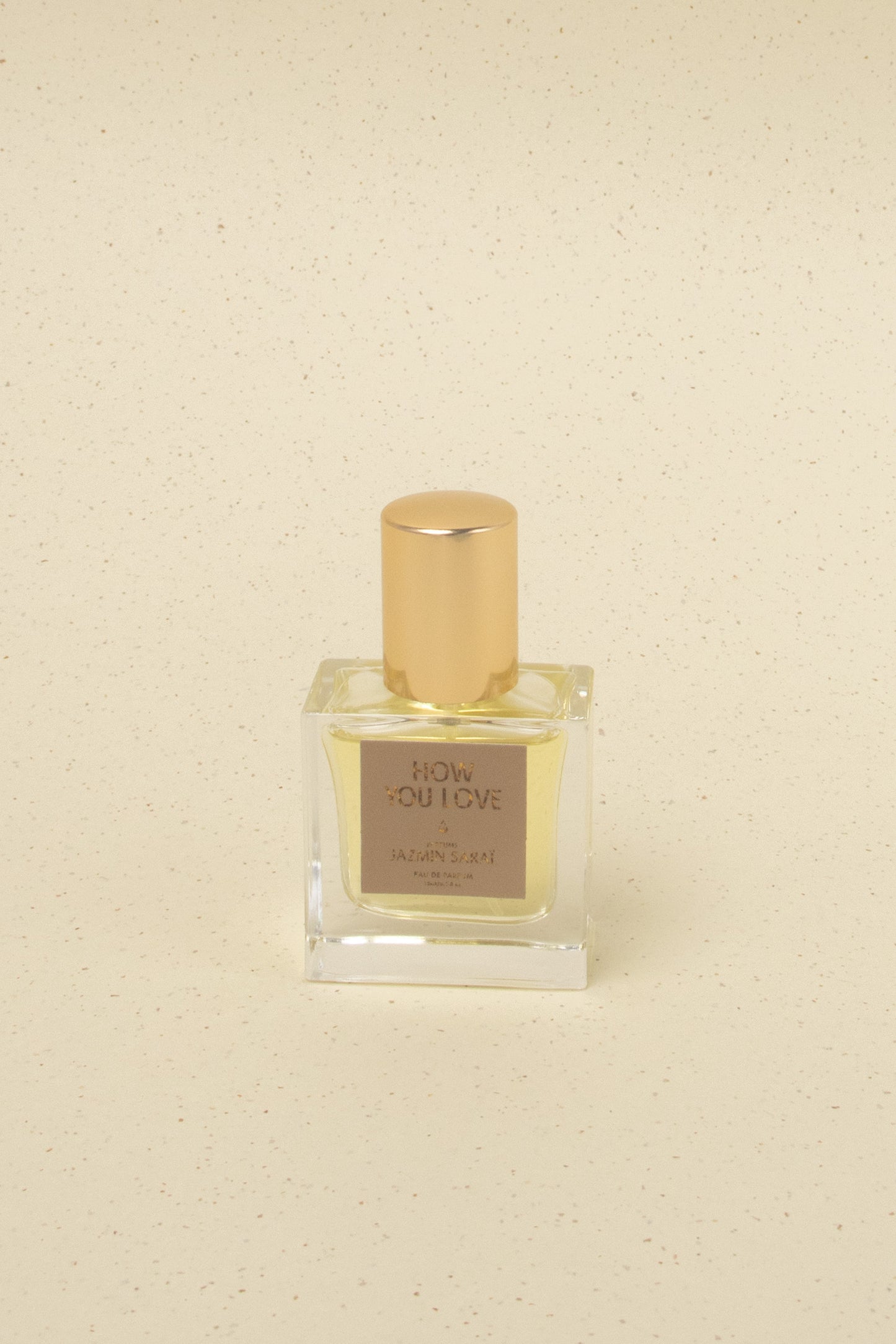Jazmin Sarai How You Love niche perfume bottle with golden cap on beige speckled background