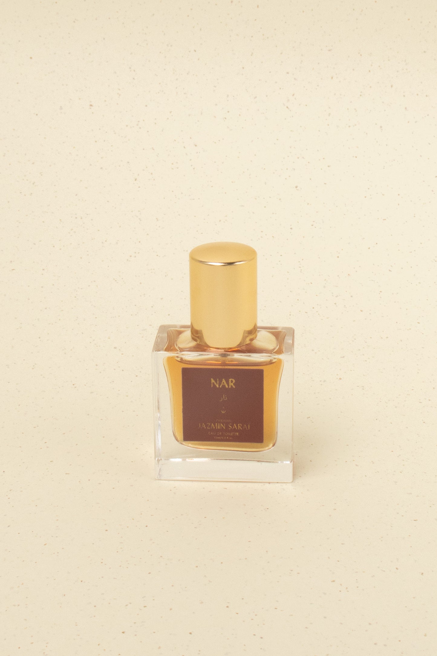 Jazmin Sarai NAR perfume bottle with golden cap on beige speckled background, niche artisan fragrance