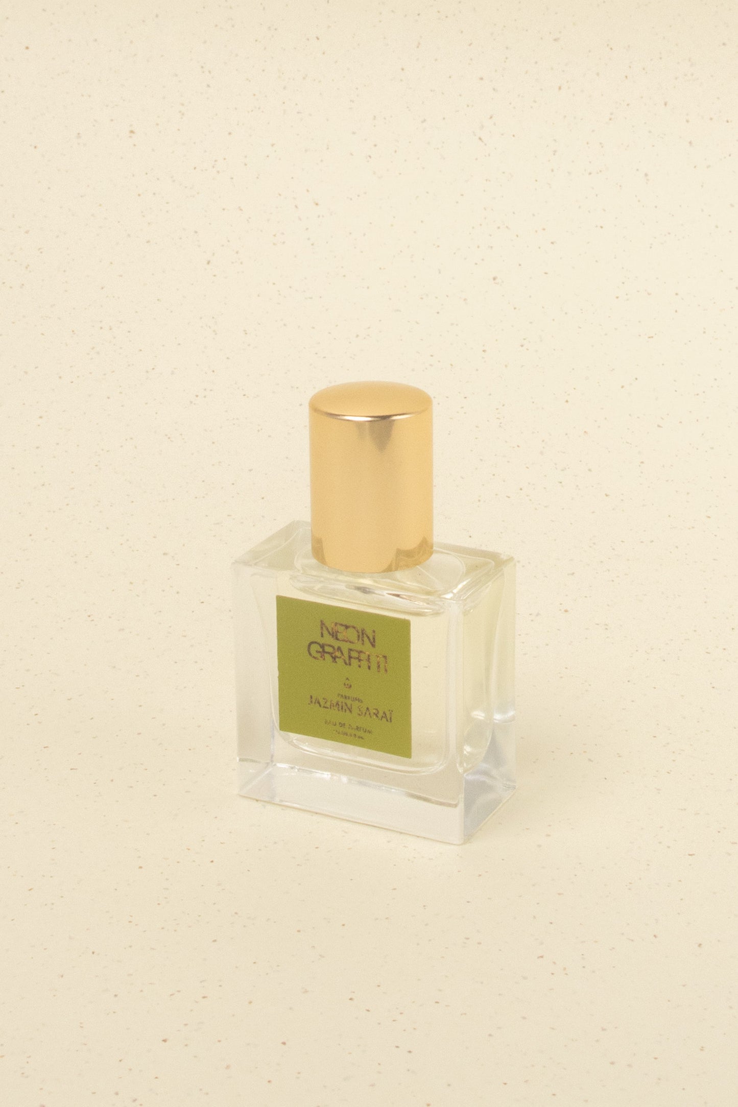 Jazmín Sarai Neon Graffiti perfume bottle with gold cap on speckled beige surface from artisan scent collection