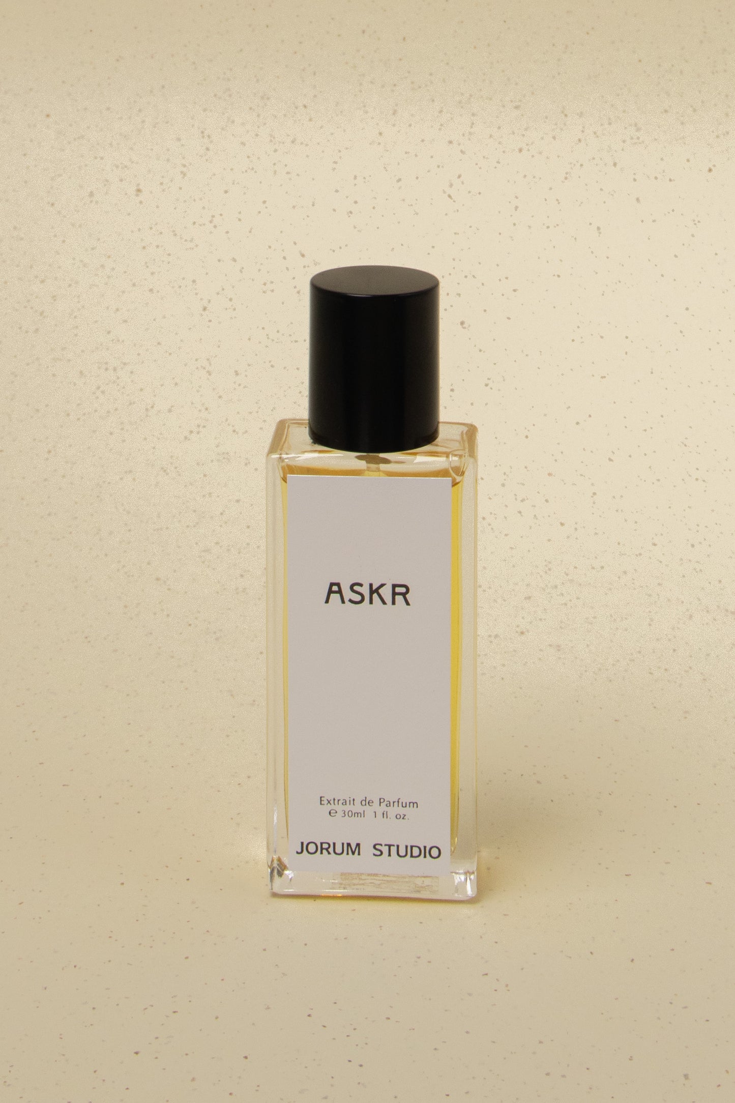 Jorum Studio ASKR perfume bottle with black cap on beige speckled surface, 30ml extrait de parfum