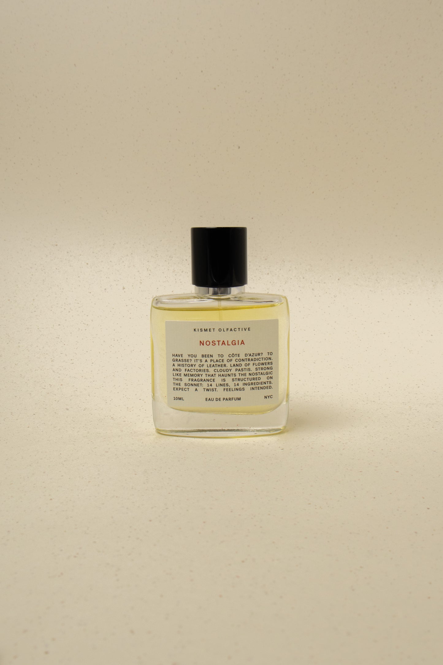 Kismet Olfactive Nostalgia eau de parfum in a clear 10ml bottle with black cap on a beige speckled background