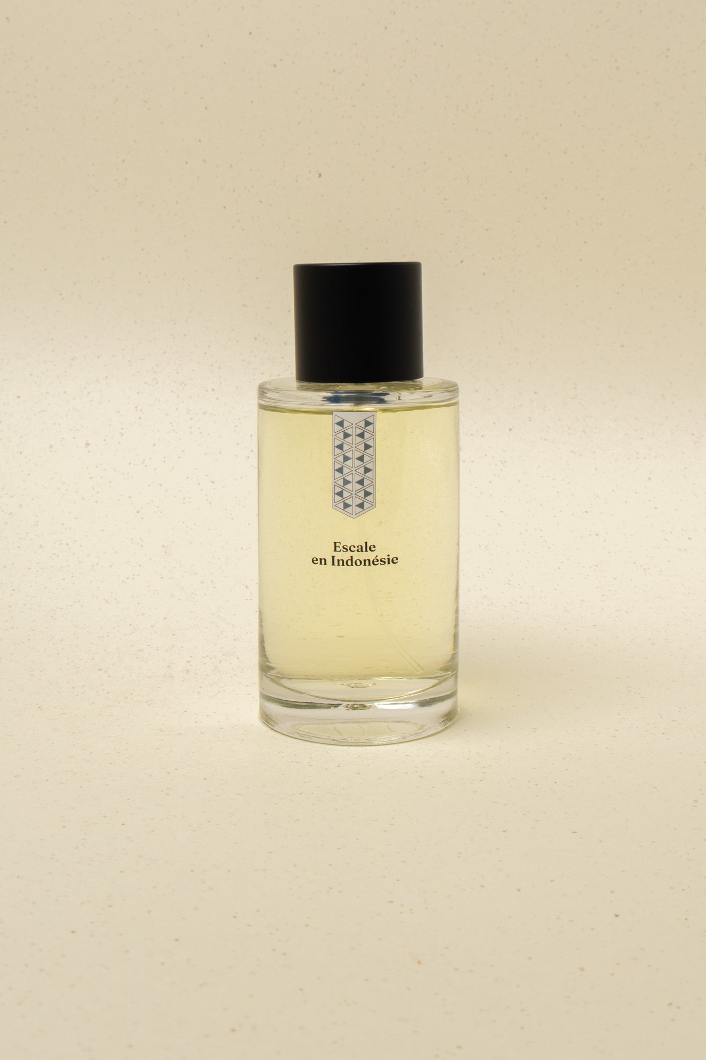 Clear glass perfume bottle labeled Escale en Indonésie with black cap on beige surface