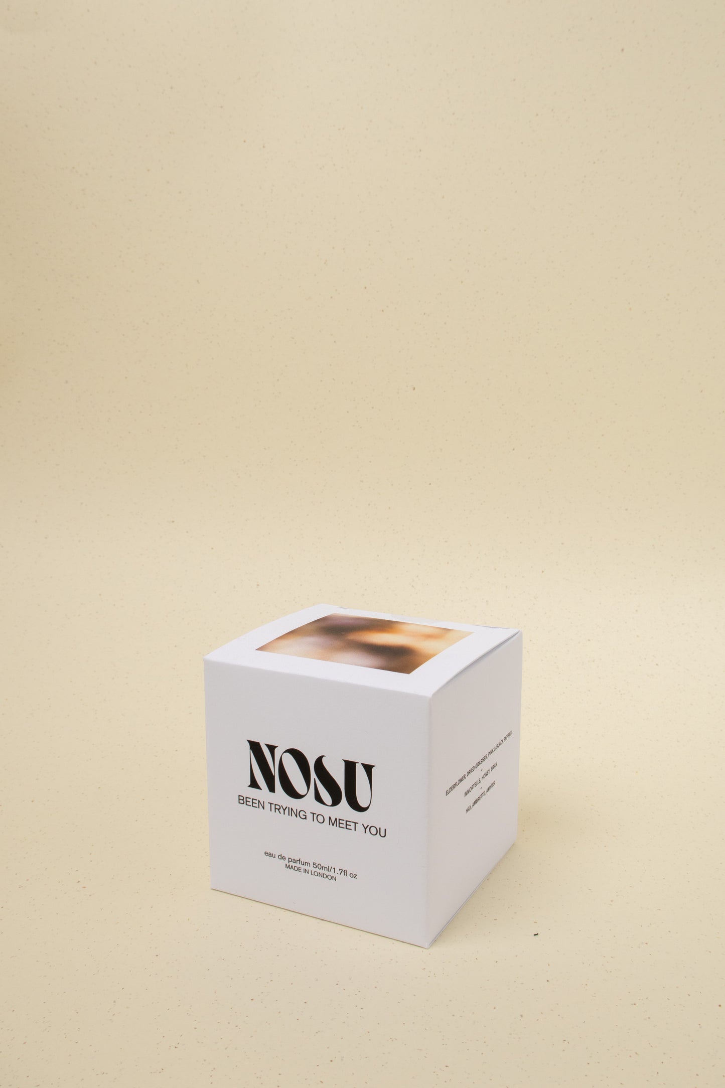 White NOSU perfume box with 'Been Trying To Meet You' text on beige speckled background