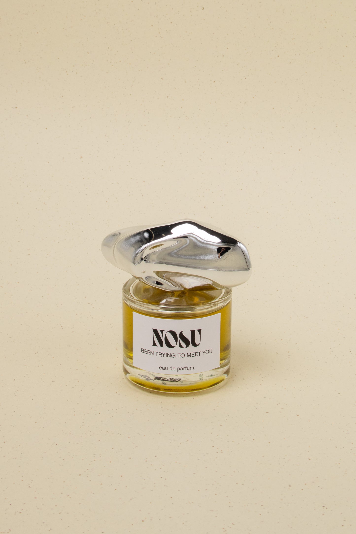 Nosu Been Trying To Meet You eau de parfum with unique silver sculpted cap on speckled beige background