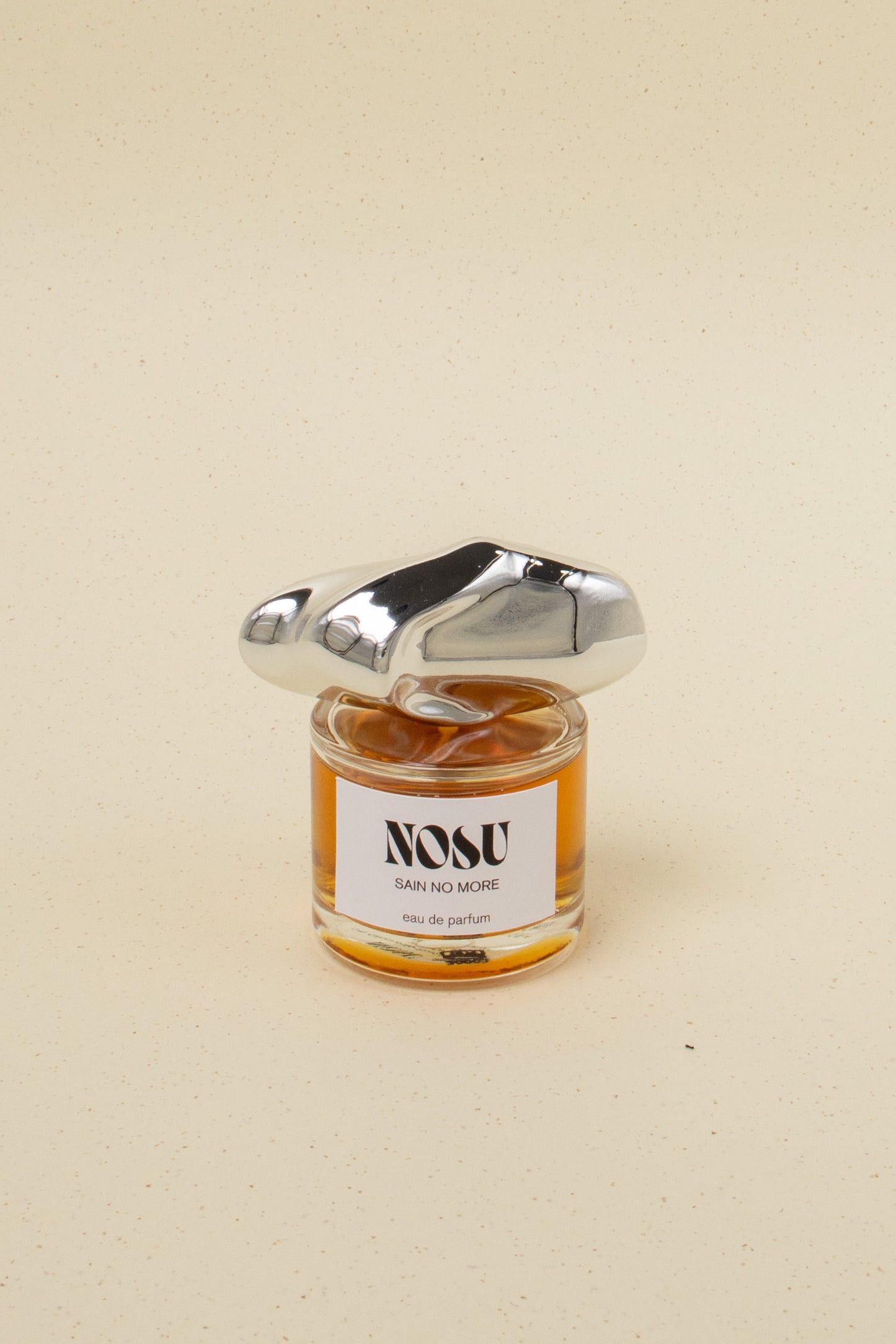 Nosu Sain No More eau de parfum bottle with unique silver cap on beige speckled background