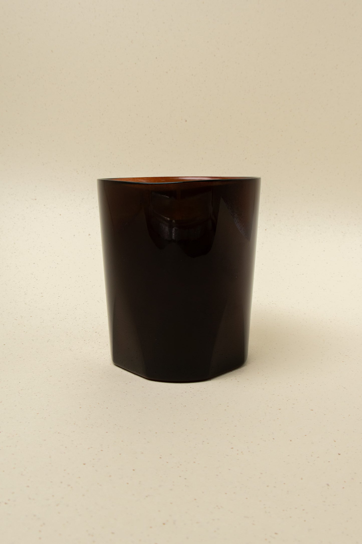 Dark brown faceted glass candle holder on a neutral speckled background